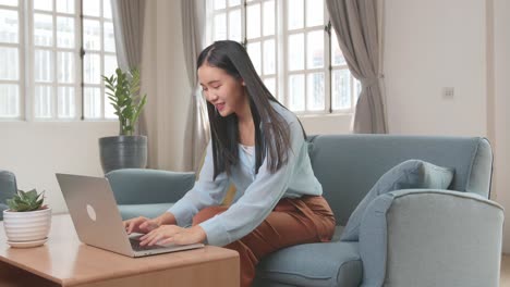 asian female working on laptop and smiling at living room while sitting on sofa, video in 4k