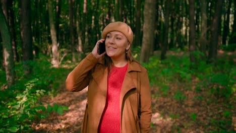 caucasian women with an overcoat and hat talking over mobile and walking in the forest trail