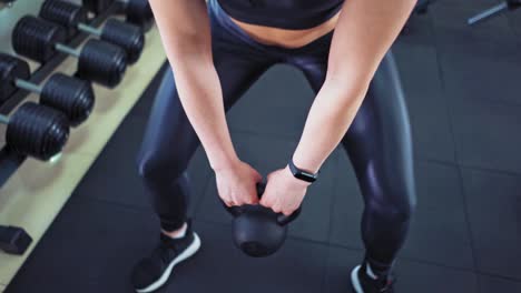 close-up of a strong musular female's body with kettlebell. athlete woman wearing black top and leggings lifting hard weight in sports club.