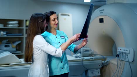 medical workers discuss the x-ray photograph. two female specialists in medical uniform examining x-ray photo on the background of new equipment in clinic.