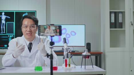 asian scientist man recording webinar, using smartphone on tripod, sitting at desk in office