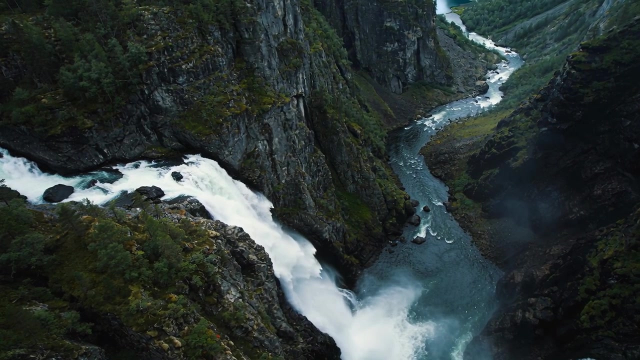 Rio caudaloso perto da borda, com cachoeira despencando de um penhasco em um desfiladeiro íngreme, criando névoa e alimentando o desfiladeiro.