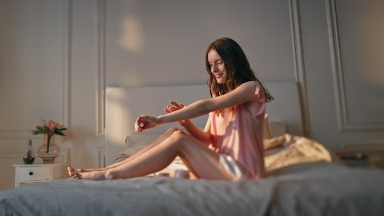 빛에서 크림을 사용하여 집에서 손을 마사지하는 소녀. 웃는 편안한 여자가 휴식을 취하고 있습니다.