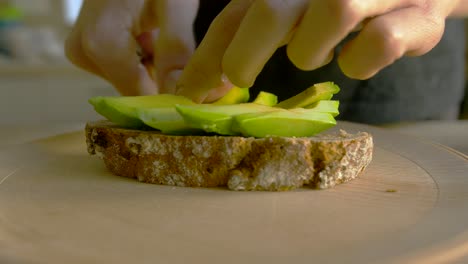 close up of young woman putting avocado on buckwheat bread