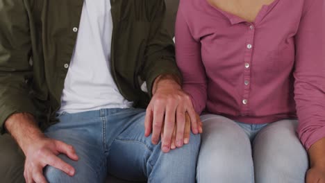 Smiling-mixed-race-couple-holding-hands-while-sitting-on-the-couch-at-vacation-home