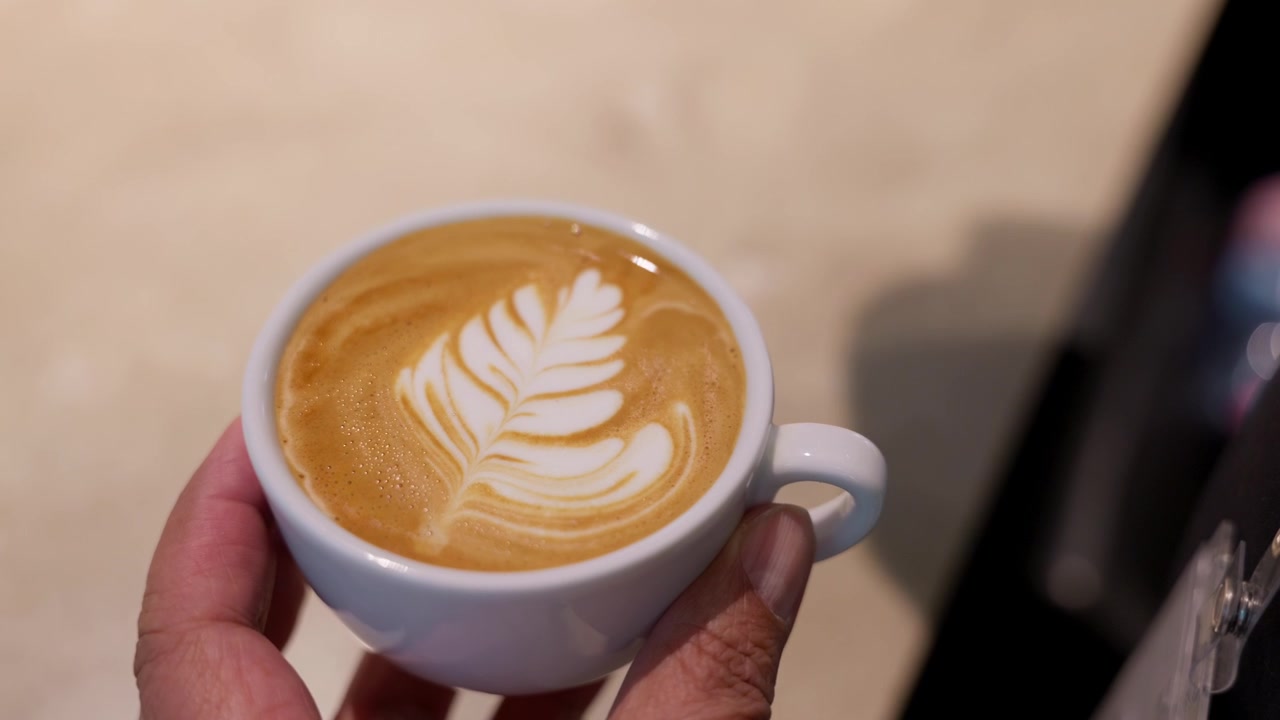 Primo piano, barista che versa il latte per creare latte art in un caffè appena preparato. Cultura del caffè di specialità, maestria, ospitalità, preparazione di bevande e concetto di stile di vita