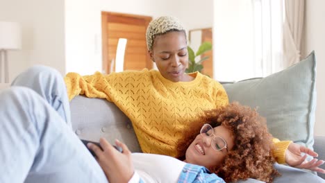 Happy-diverse-female-lesbian-couple-talking-and-using-tablet-in-living-room-in-slow-motion