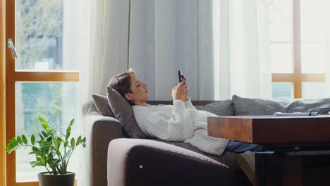 mujer relajándose en el sofá, usando el teléfono