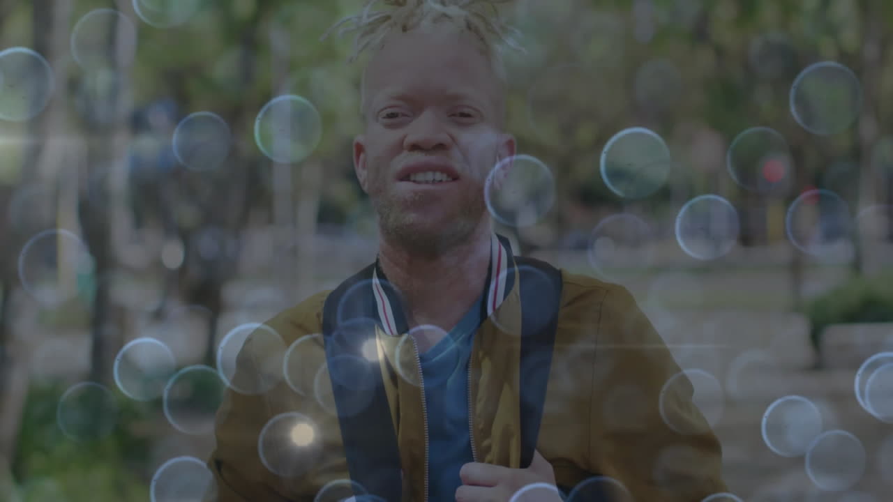 Male student standing in yellow jacket on park path, floating bokeh overlays enhancing education