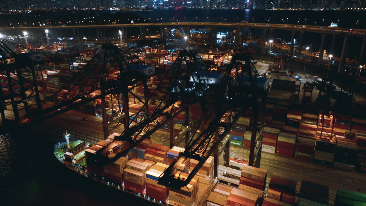 Gantry cranes working at a container vessel while traffic drives over the high bridge in de background with a view on the skyline of Hong Kong