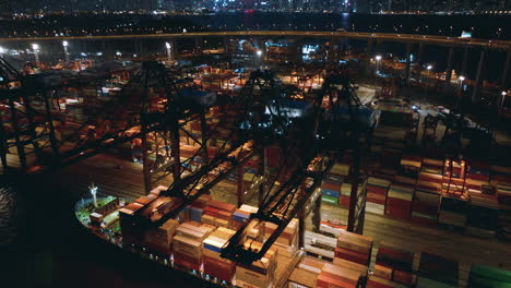 gantry cranes working at a container vessel while traffic drives over the high bridge in de background with a view on the skyline of hong kong