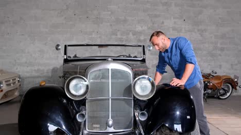 man inspecting a classic black convertible car in a garage