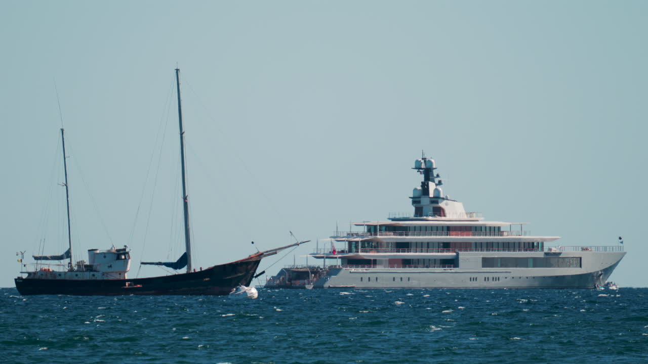 Contrast between an old sailboat and a modern luxury yacht floating on calm Mediterranean waters
