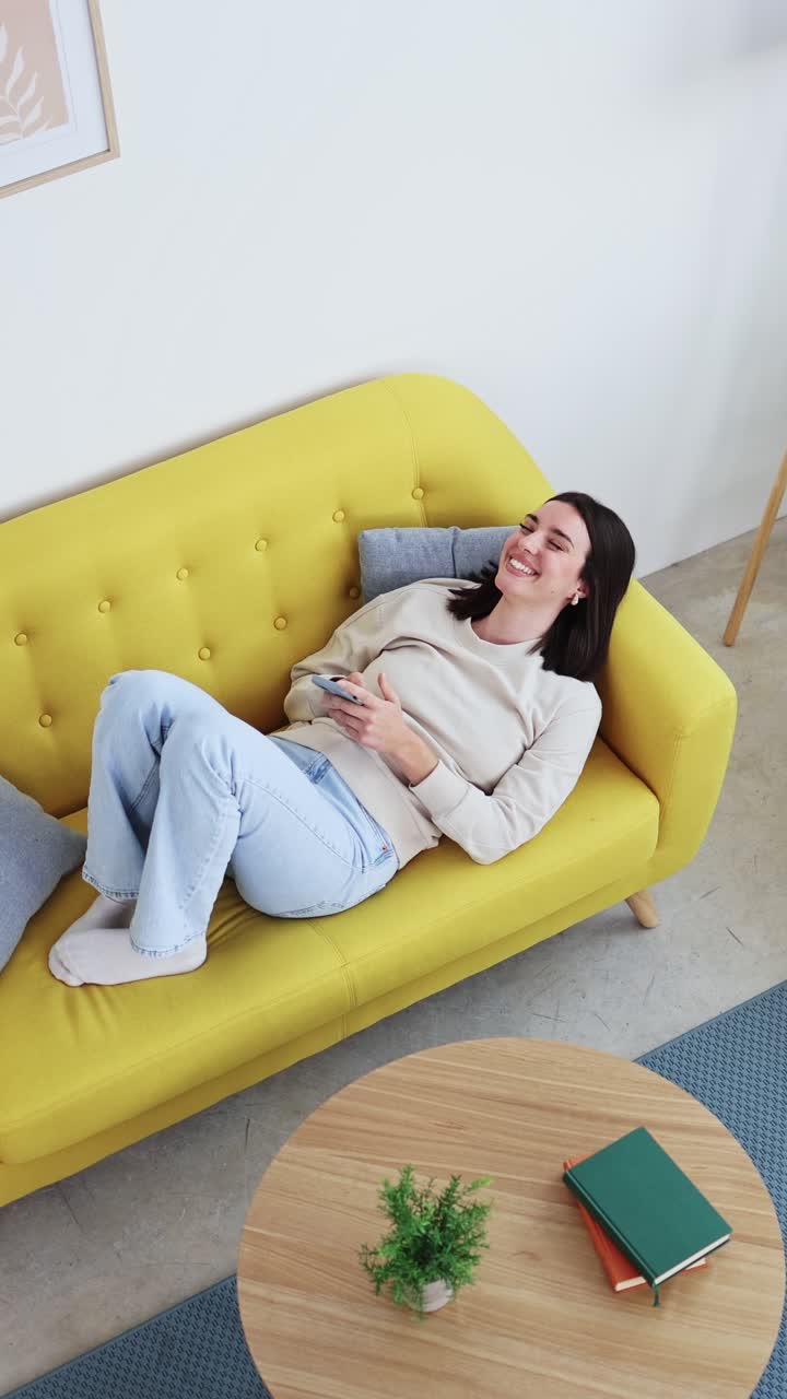 Giovane donna felice che si rilassa sul divano e usa lo smartphone