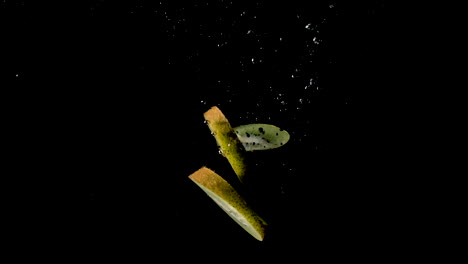 Sliced-kiwis-dropped-in-water-on-black-background,-slow-motion-close-up