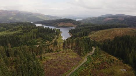 a sweeping aerial shot rises to reveal a calm scottish loch nestled in a huge lush forest