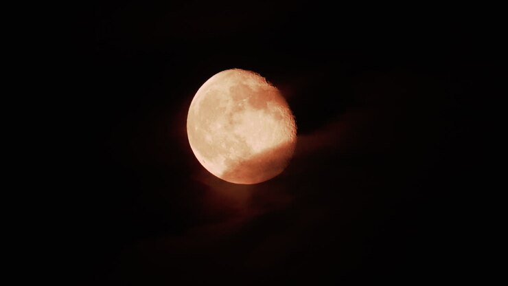 A golden full moon partially covered by drifting clouds in the night sky