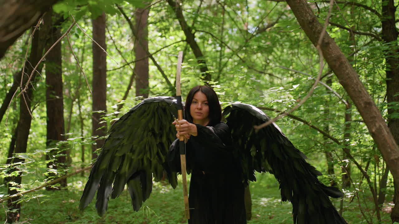 Mysterious black fairy with large dark wings stands in lush green forest holding wooden staff, sunlight filtering through leaves, mystical atmosphere