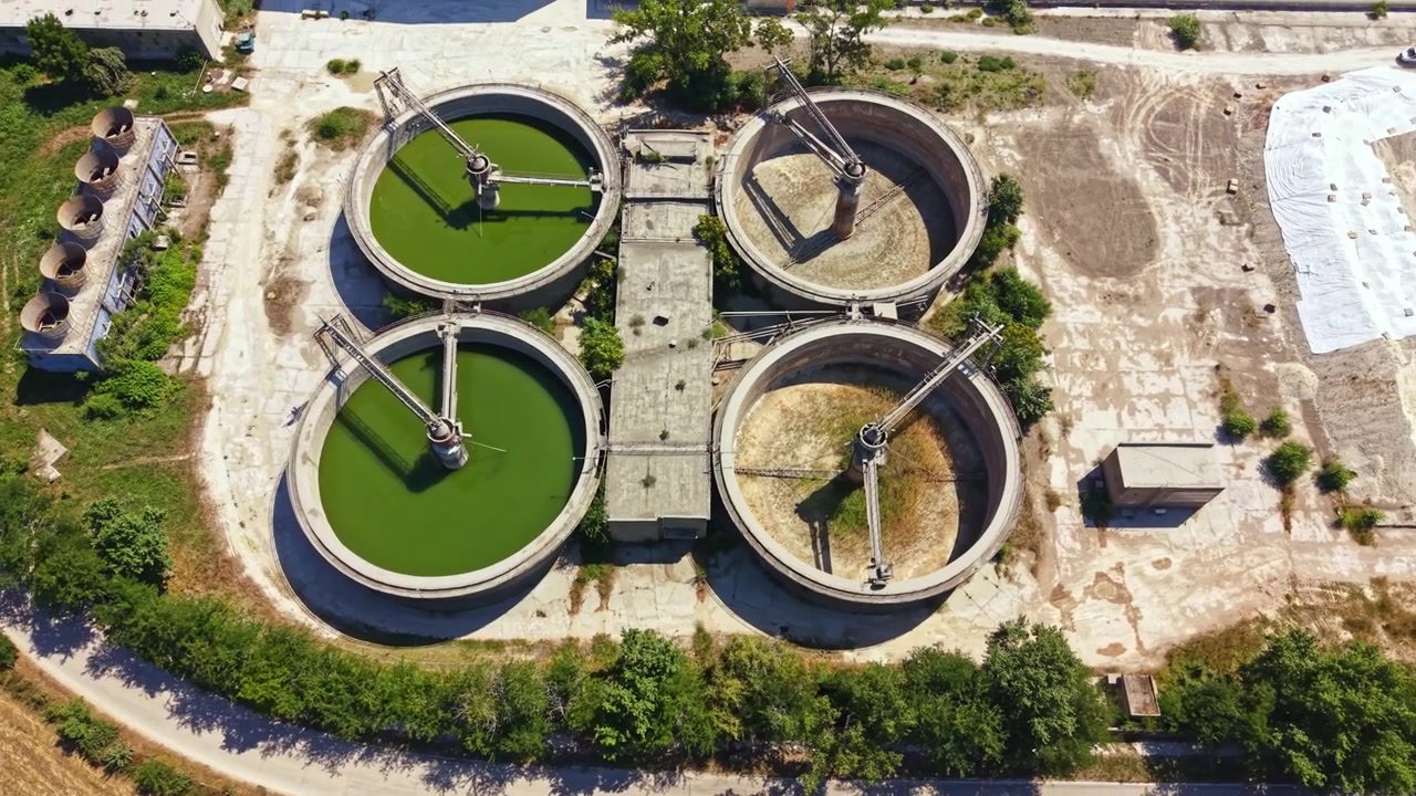 Old water treatment facility near a river with three large circular tanks and surrounding greenery