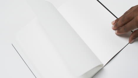 video of hand of african american man holding book with blank pages, copy space on white background