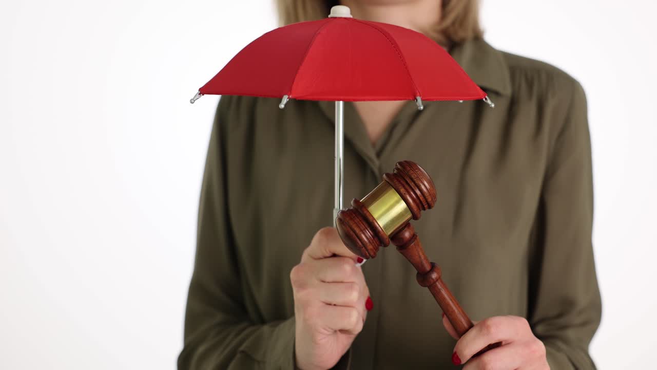 Donna che tiene un martelletto da giudice in legno sotto un ombrello rosso in studio
