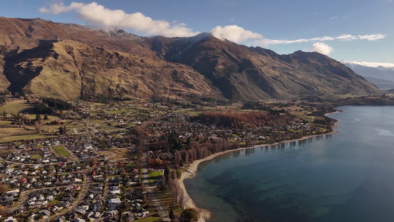 Scenic aerial of Wanaka town on beautiful lakefront with large mountains in background under blue sky, South Island, New Zealand