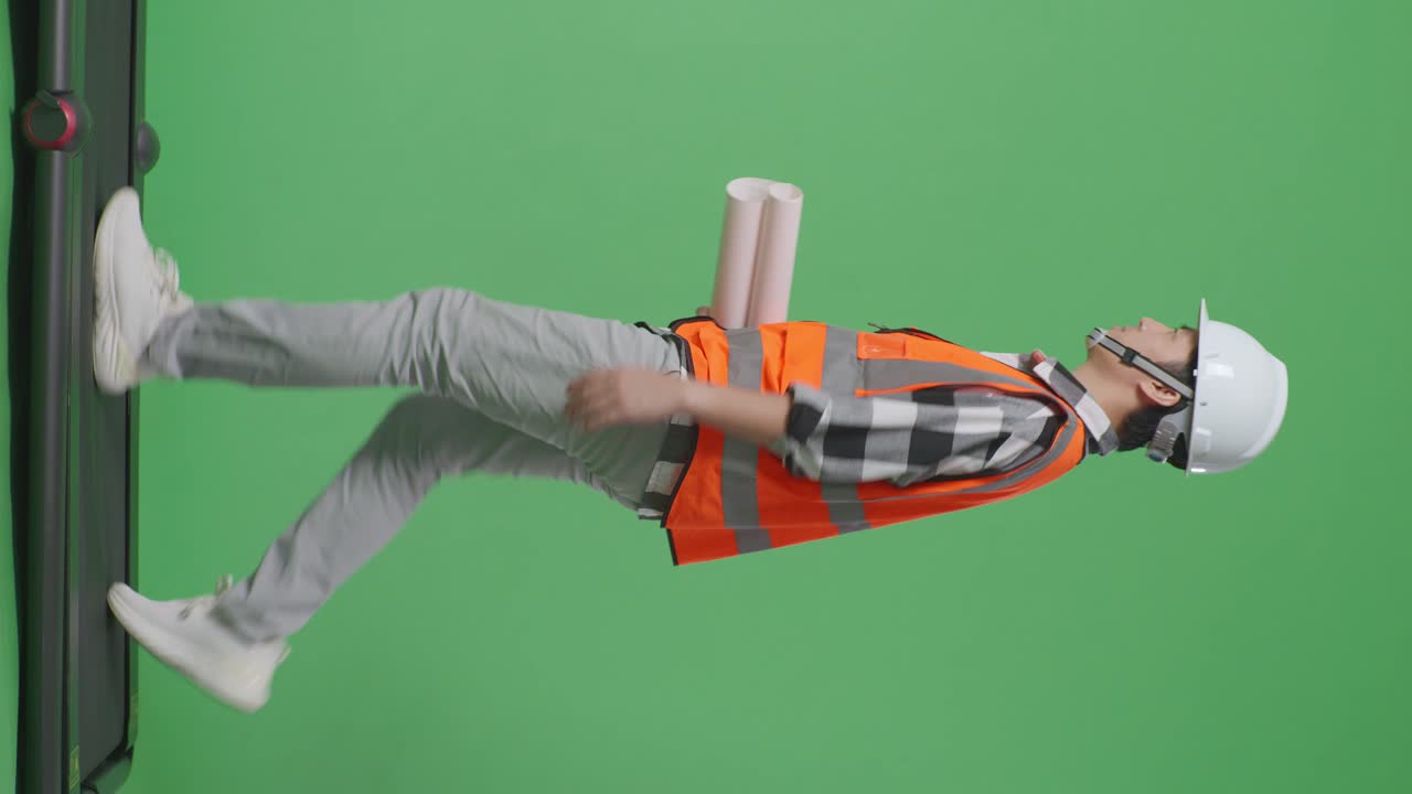 안전 헬을 입은 아시아 남성 엔지니어가 손에 블루프린트를 들고 녹색 스크린 배경 스튜디오에서 는 동안 주위를 둘러보고 있습니다.