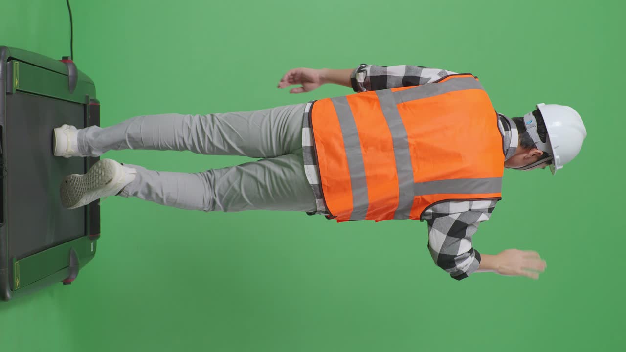 안전 헬을 입은 아시아 남성 엔지니어가 녹색 스크린 배경 스튜디오에서 는 동안 손을 흔들고 있습니다.