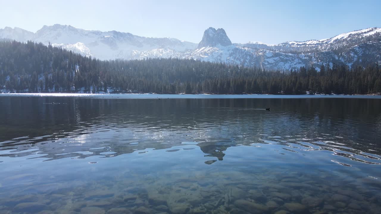 drone volando cerca del agua hacia montañas nevadas que ascienden lentamente en los gigantescos lagos de california