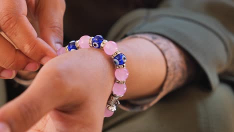 close-up of a person adjusting a pink and blue beaded bracelet with evil eye charms on their wrist