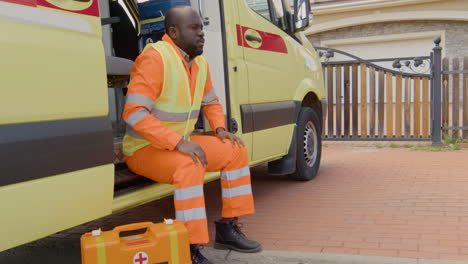 sad ambulance driver waiting on the ambulance at the entrance of a house