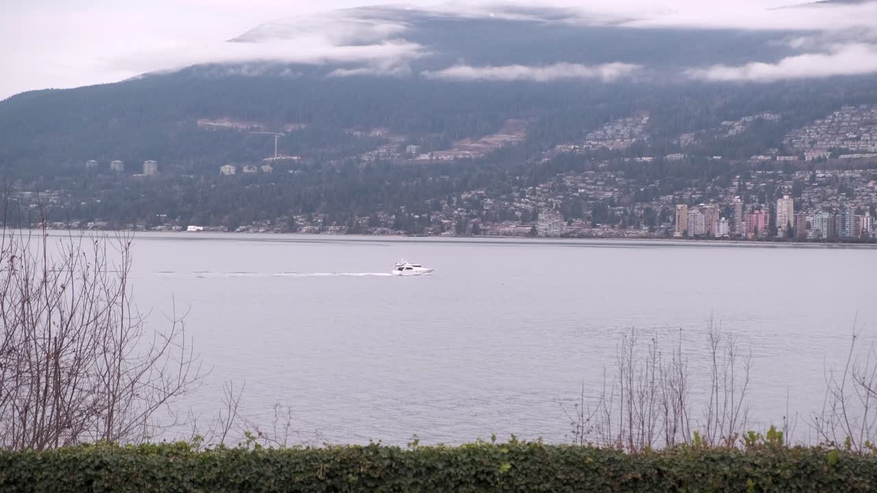 pequeño bote blanco cruzando el marco de izquierda a derecha en un día nublado de invierno con una montaña y edificios en el fondo
