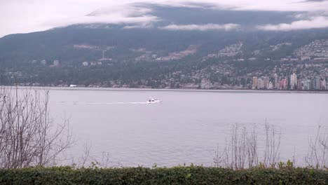small white boat crossing the frame from left to right on a cloudy winter day with a mountain and buildings in the background
