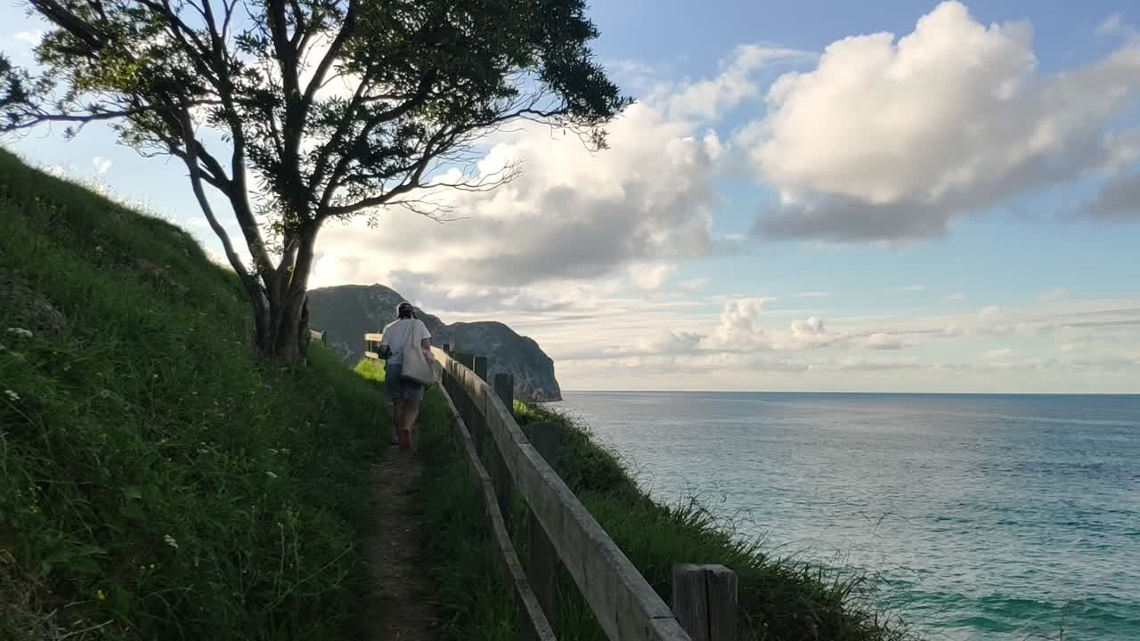 Woman walks barefoot on a cliff path at Bretones Beach, Asturias, at sunset