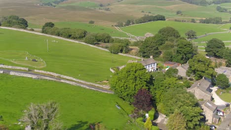 Sideways-moving-drone-footage-in-the-beautiful-rural-village-of-Selside,-Yorkshire,-UK-tracking-motorbikes-on-a-country-lane-with-fields,-farmland-and-hills-in-the-distance-on-a-sunny-summer-day