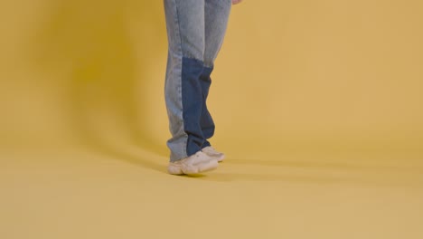 close up on legs and feet of woman having fun dancing against yellow studio background 2