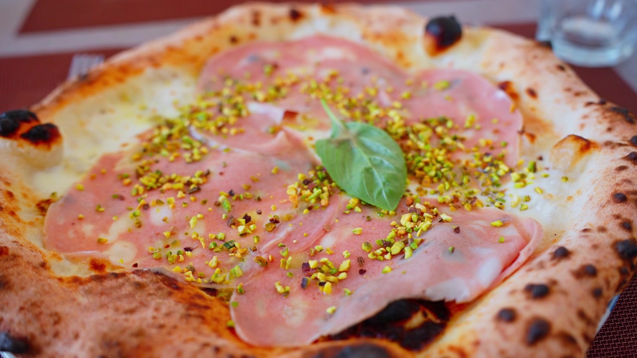 Pizza napoletana di Pompei guarnita con mortadella, pistacchi tritati, formaggio fuso, basilico e una crosta carbonizzata cotta nel forno a legna.