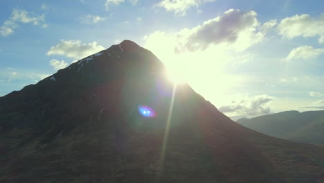 el sol que aparece detrás de la montaña buachaille etive mor cerca de glencoe en las tierras altas escocesas, escocia