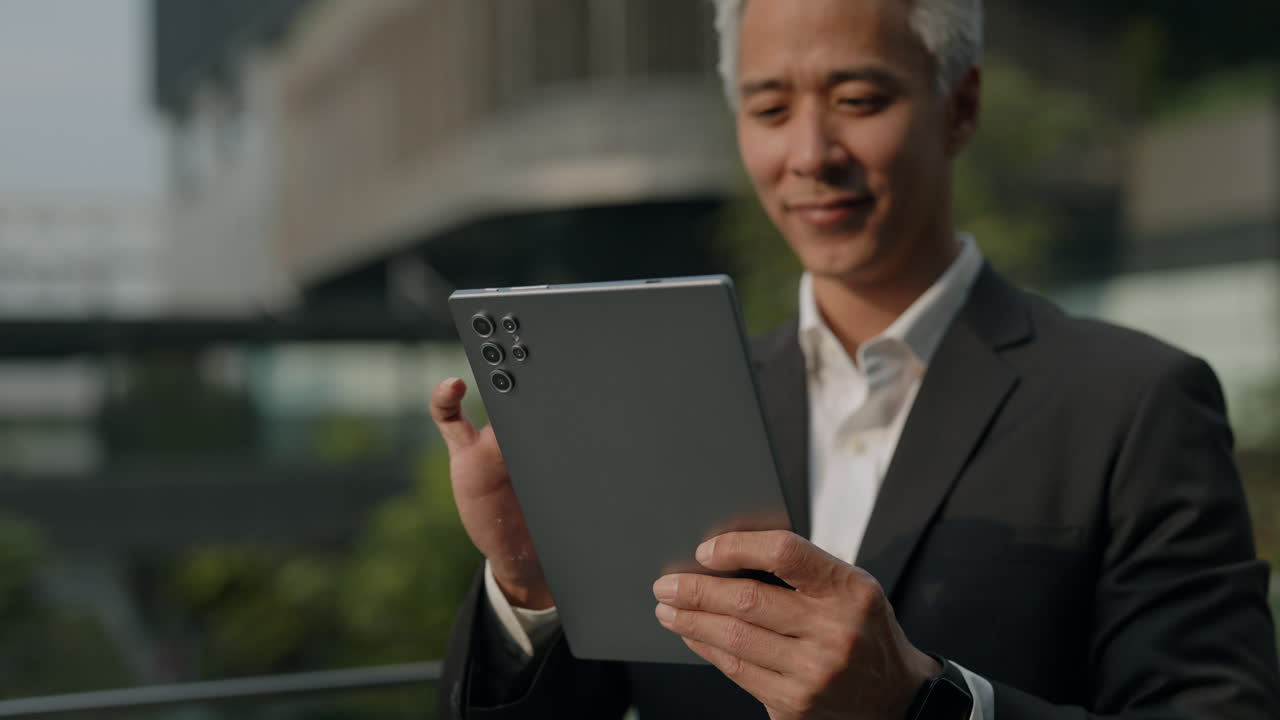 Smilende asiatisk forretningsmann bruker digitalt nettbrett utendørs