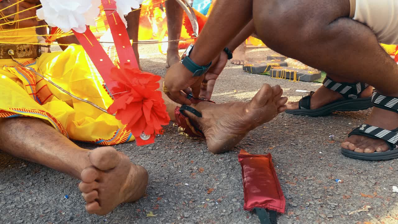 A devotee is being assisted in a sacred ritual, involving the fastening of symbolic elements to his legs as part of a traditional Hindu religious practice demonstrating faith, endurance, and devotion