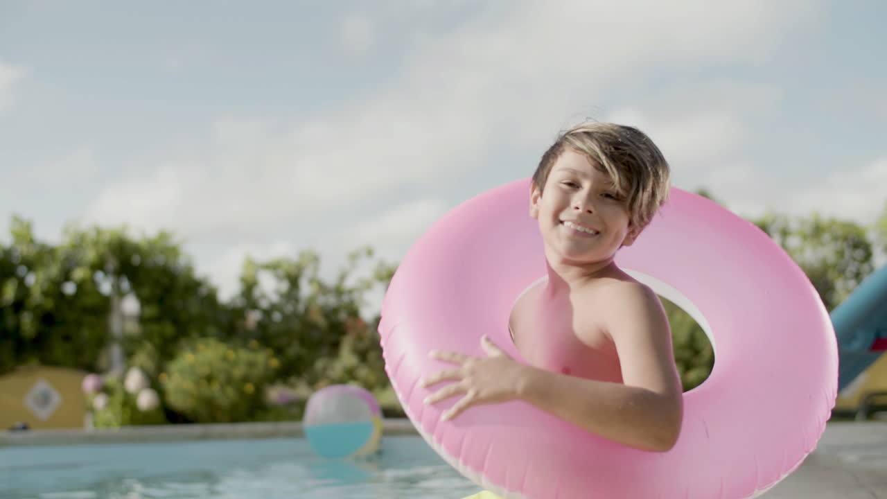 un niño con un anillo inflable, sentado a la orilla de la piscina y sonriendo.