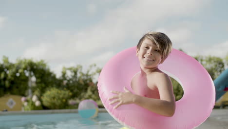 Niño-Con-Anillo-Inflable,-Sentado-Junto-A-La-Piscina-Y-Sonriendo.