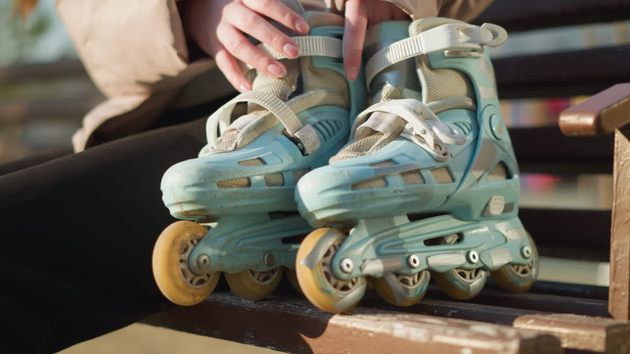 A close-up shot of a person walking to a park bench and sitting down, placing their rollerblades beside them. The bench is in focus, with the person remaining faceless