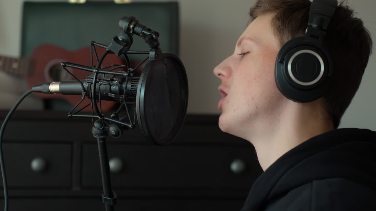 Close-up of Young Male Singer Recording Vocals in Home Studio Setup with Headphones