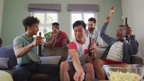 happy diverse male friends watching tv and drinking beer in living room