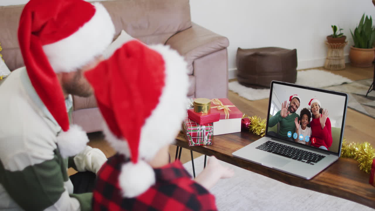 padre y hijo caucásicos usando sombreros de santa en una videochat portátil durante la navidad en casa