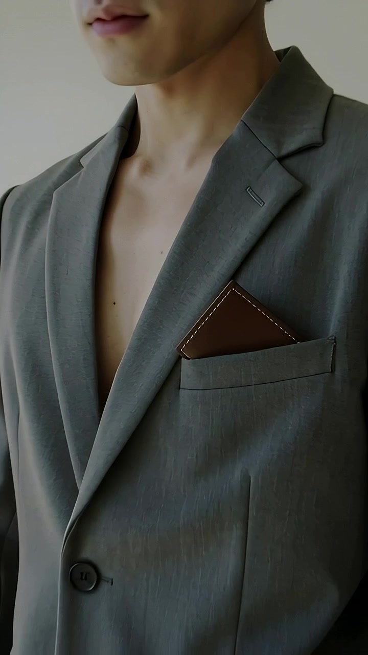 Vertical video: Bare man in blazer tucking cardholder into pocket in studio, hand reaching posing