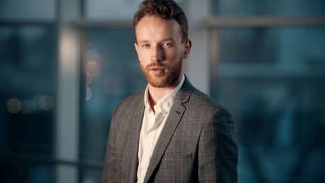 Portrait-of-a-stylish-smiling-young-man-on-a-background-of-night-city-in-the-office