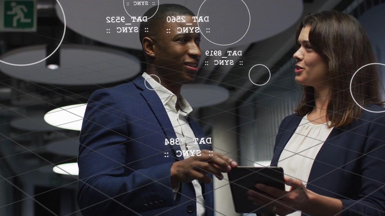 Man tapping tablet, woman following tech data in corridor, AR markers floating over tablet syncing