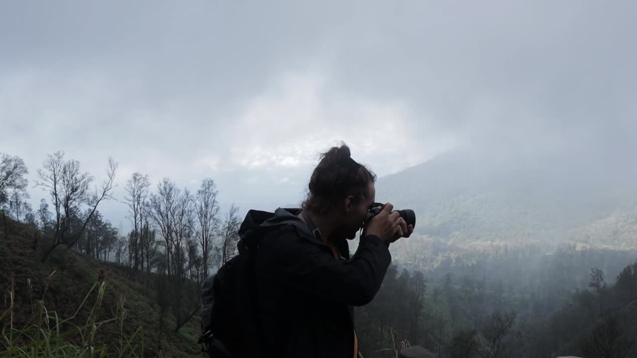 Caucasian backpacker man taking photo in foggy smoke forest mountain